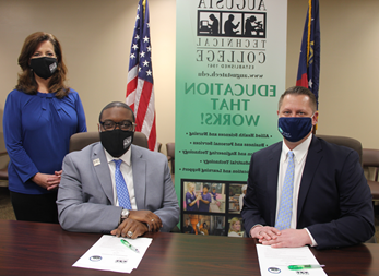 Caucasian male wearing a blue face mask, blue suit jacket, white collared shirt, light blue tie, hands folded while sitting down at a table, white paper in front of him with a green pen; African American male wearing a black Augusta Tech branded face mask, light gray suit, silver Augusta Tech lapel pin, white collared shirt, blue/purple tie, silver watch, hands folded white sitting at a brown table, white papers on brown table in front of him with a green pen; Caucasian female standing wearing a black Augusta Tech branded face mask, blue shirt, hands folded together, black pants, background features an American flag, the state of Georgia flag, large retractable banner showing old Augusta Tech logo, verbiage reads: y5pxqrrn.luxury-rehab-centers.com, Education That Works; bulleted list reads Allied Health Sciences and Nursing, Business and Personal Services, and Engineering Technology, Industrial Technology, and Learning Support, photos underneath the bulleted list.